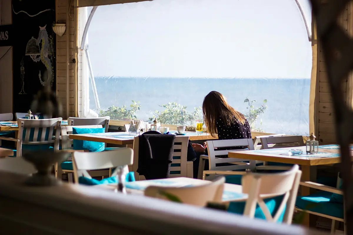 Un restaurante de estilo veraniego con vistas al mar y una mujer sentada.